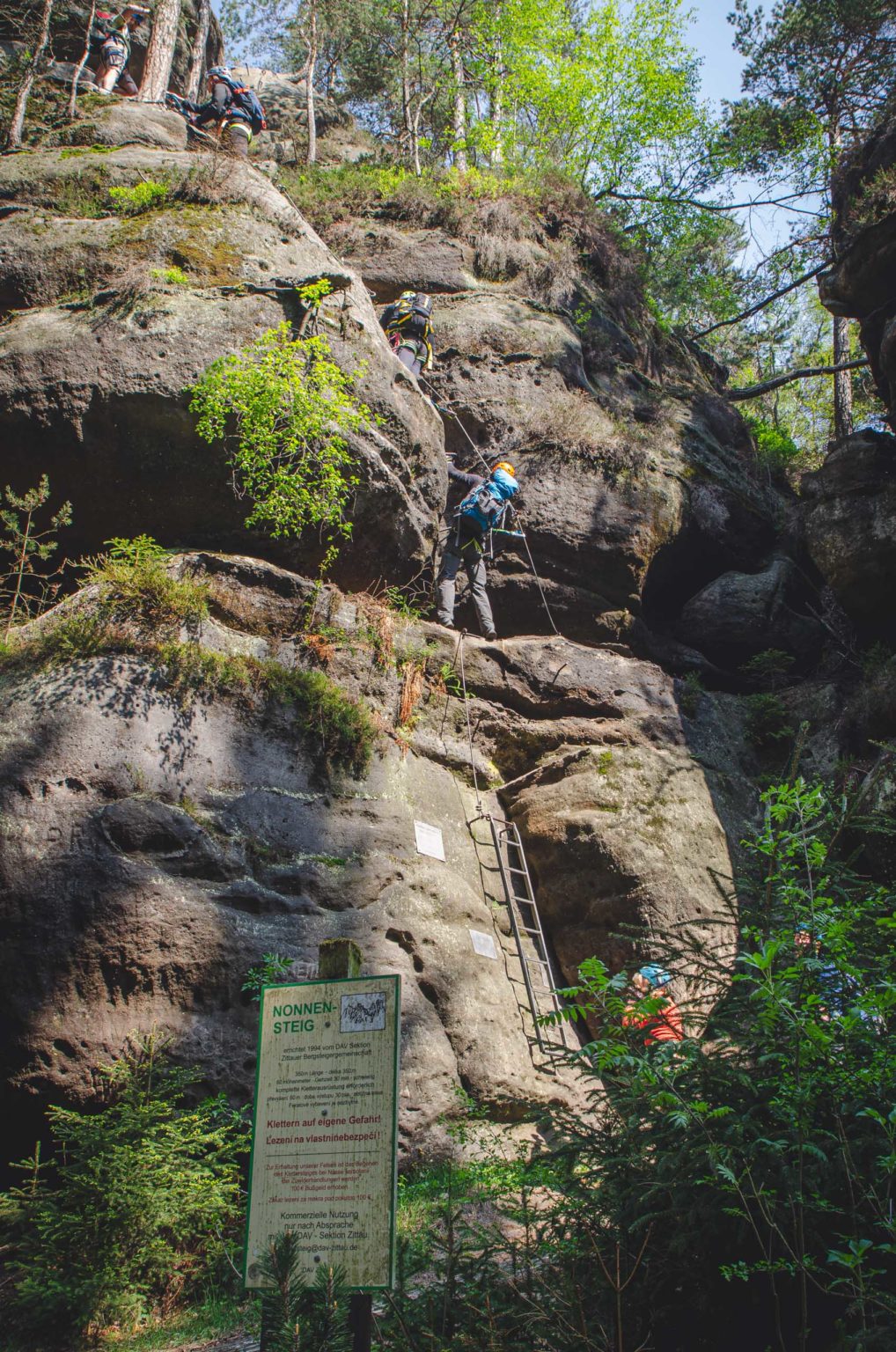 Mężczyzna wspina się po skałach. Przed skałami stoi tablica