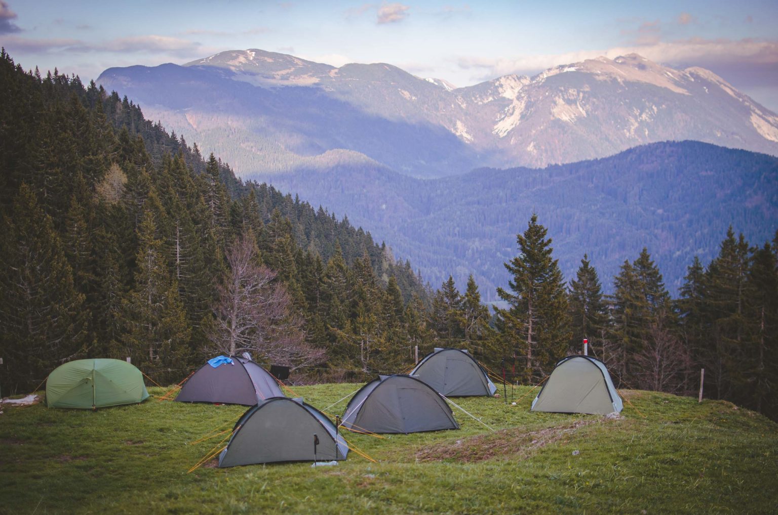 Sześć namiotów rozłożonych na polanie z widokiem na Karawanki