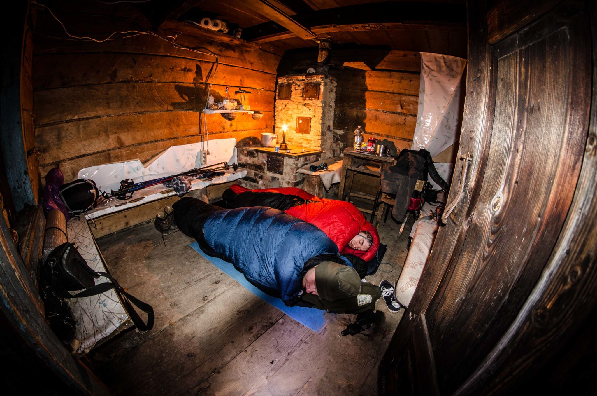 Dwóch mężczyzn w śpiworach leży na podłodze w bacówce w górach