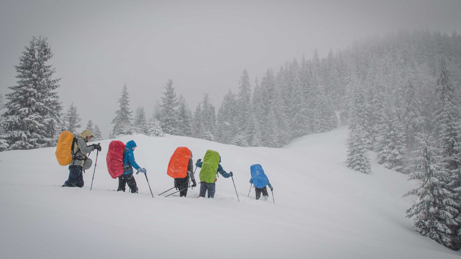 Grupa osób idzie w głębokim śniegu w górach