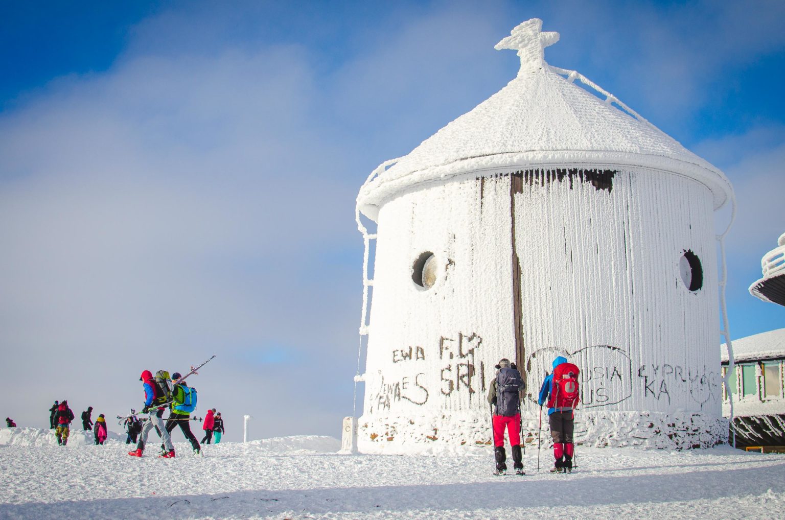 Osoby stoją przy kaplicy na szczycie Śnieżki