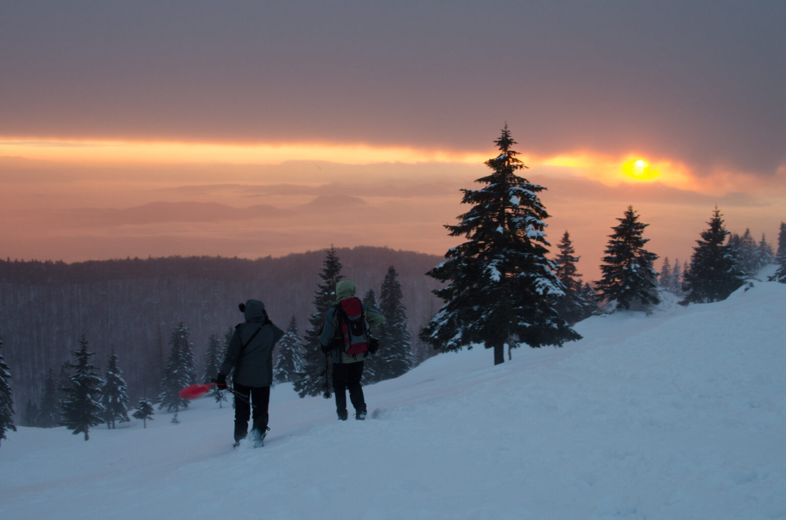 Dwoje turystów idzie po śniegu, w tle zachód słońca