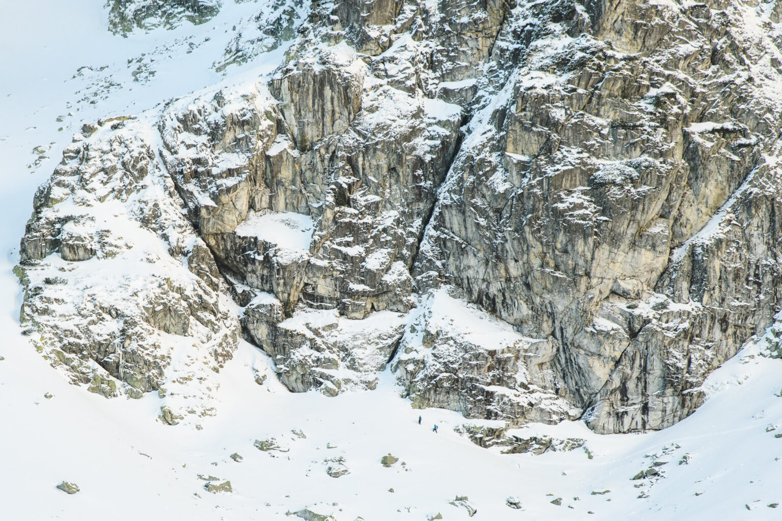 Dwóch taterników stoi na śniegu u podstawy ściany Mnicha